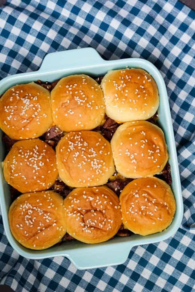 nine sliders with sesame seeds on top in a blue baking dish