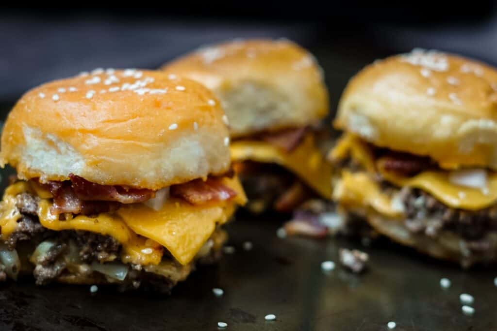 three bacon cheeseburger sliders on a dark pan