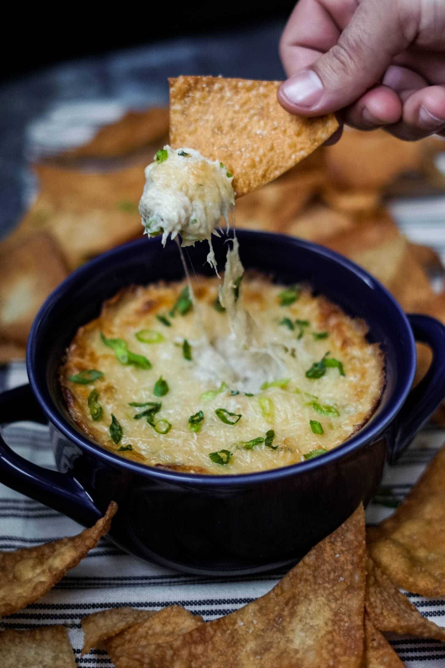 cheese pull of crab rangoon dip in a blue bowl with fried wonton chips