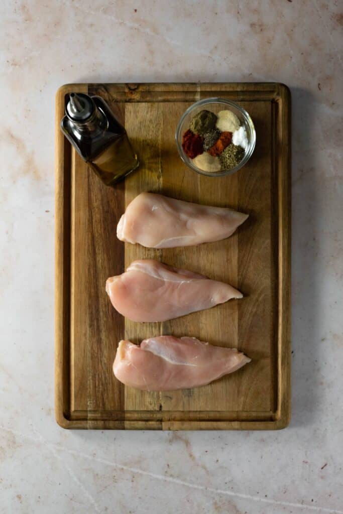 Ingredients and seasonings for chicken breasts laid out on a cutting board