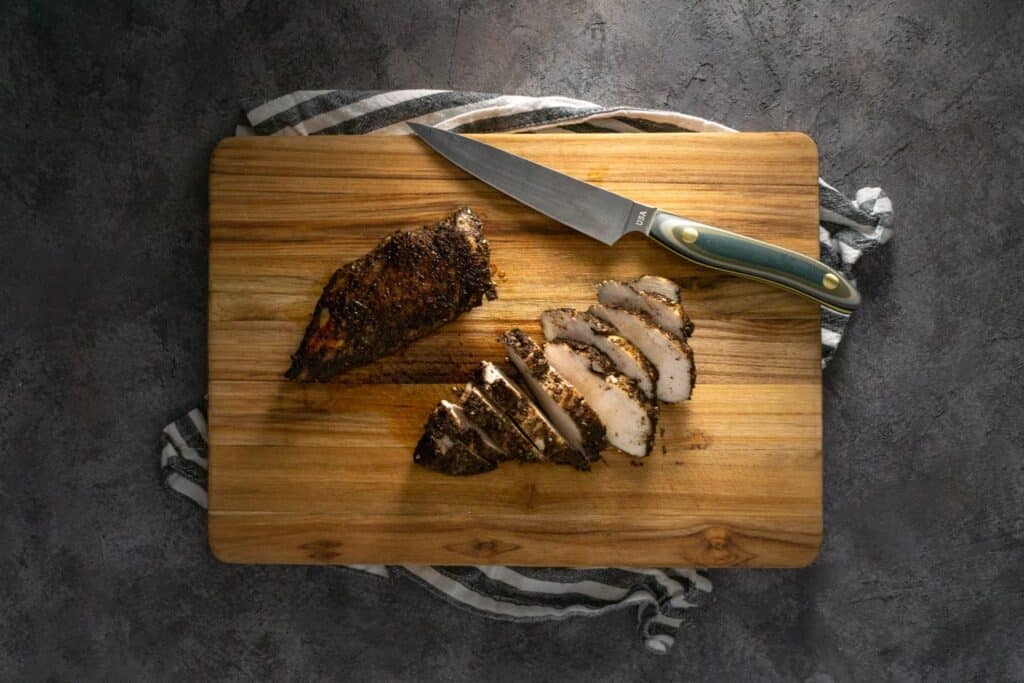seared chicken sliced on a cutting board with a knife
