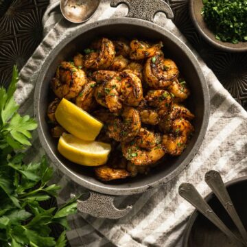 A bowl of blackened shrimp with lemon wedges and parsley.