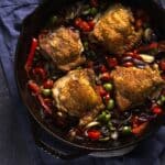 chicken thighs with crispy skin with olives and peppers in a cast iron skillet