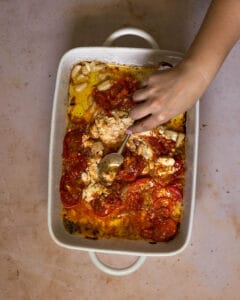 mixing roasted tomatoes and goat cheese in a white baking dish