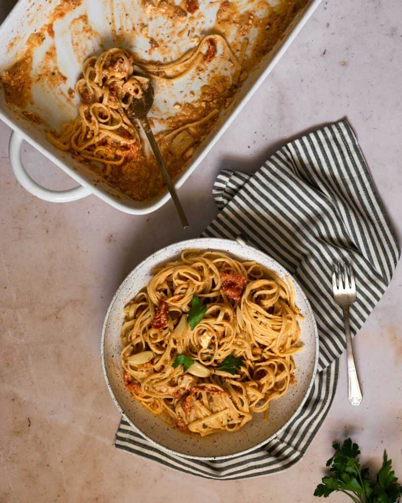 a baking dish with goat cheese and tomato pasta and a bowl full of pasta