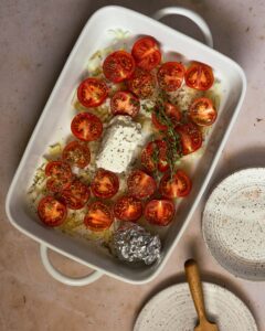 a white baking dish with goat cheese, tomatoes, thyme and olive oil