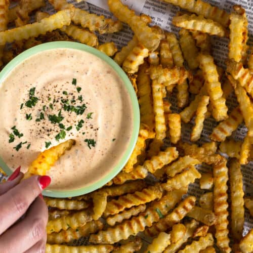 hand dipping into cajun garlic aioli on a tray of crinkle cut fries