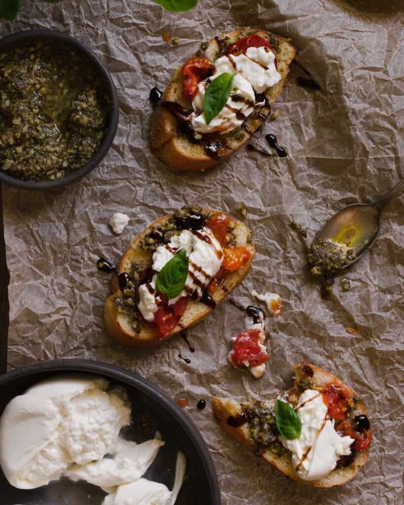 Burrata bruschetta assembled on parchment paper with roasted tomatoes, creamy burrata, pesto, and balsamic glaze