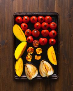 tomatoes, mango, onion, and habanero roasted on a baking sheet on a wooden table