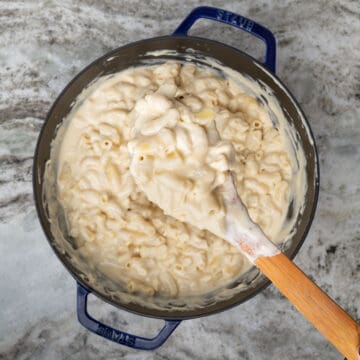 large pot of dutch oven mac and cheese and a spoon holding a scoop