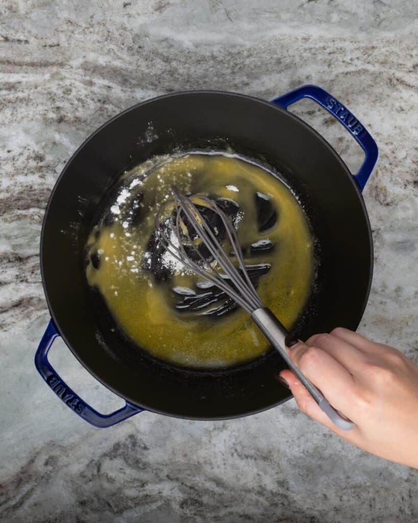 whisking flour into melted butter in a blue dutch oven