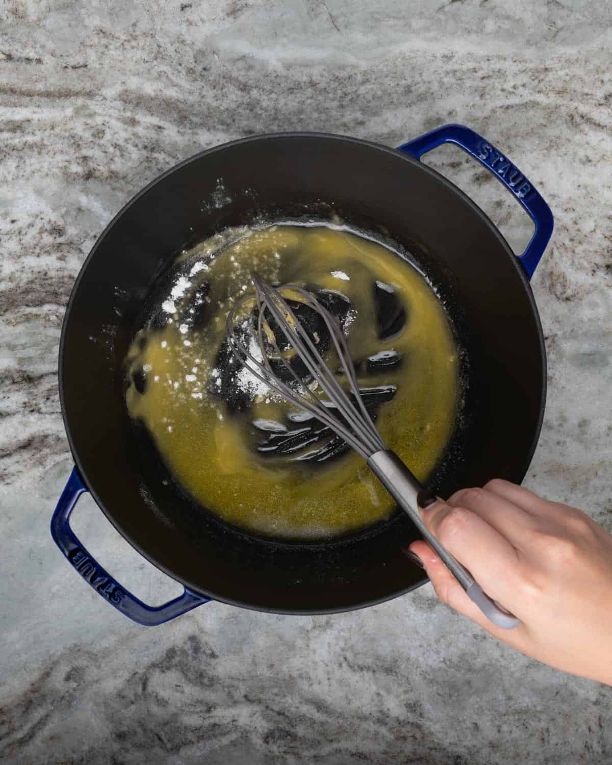 Whisking flour into melted butter in a blue dutch oven.