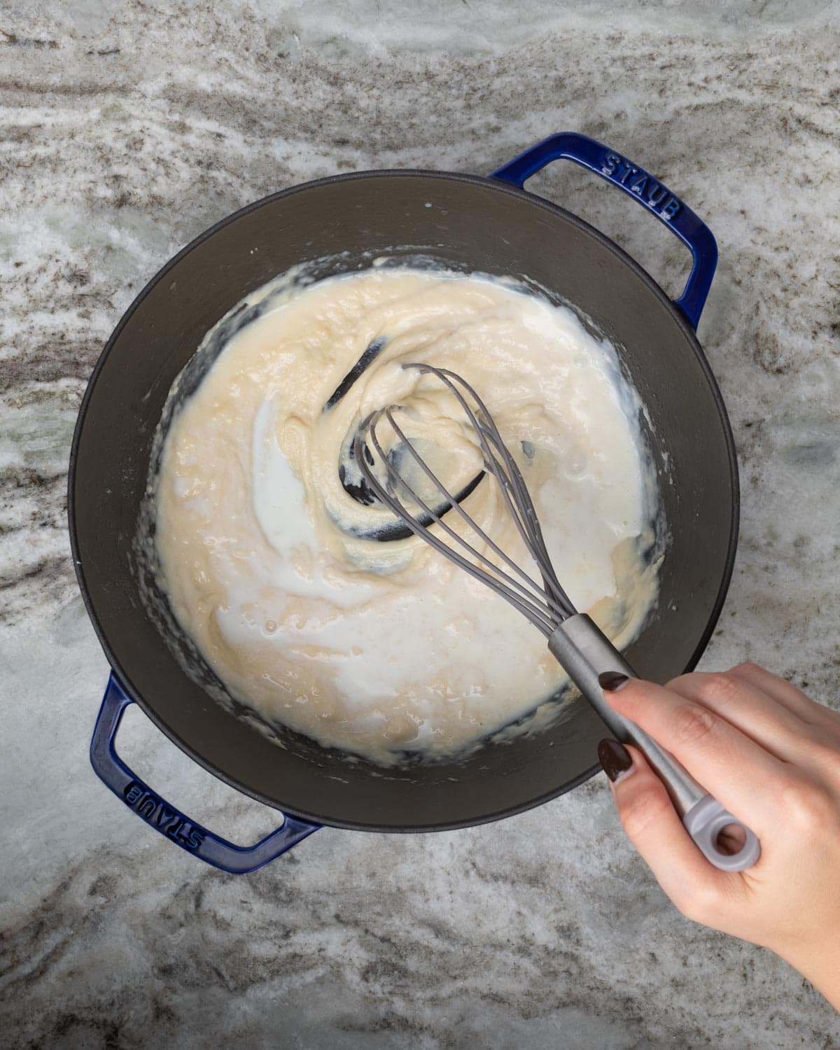 A hand whisking a blonde roux in a dutch oven.
