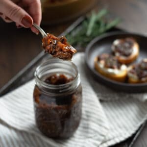 a hand holding a spoon full of caramelized onions over a jar full of them
