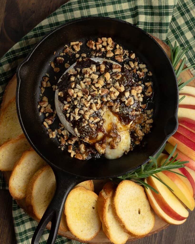 melted baked brie with fig jam in a cast iron skillet with apple slices and baguettes