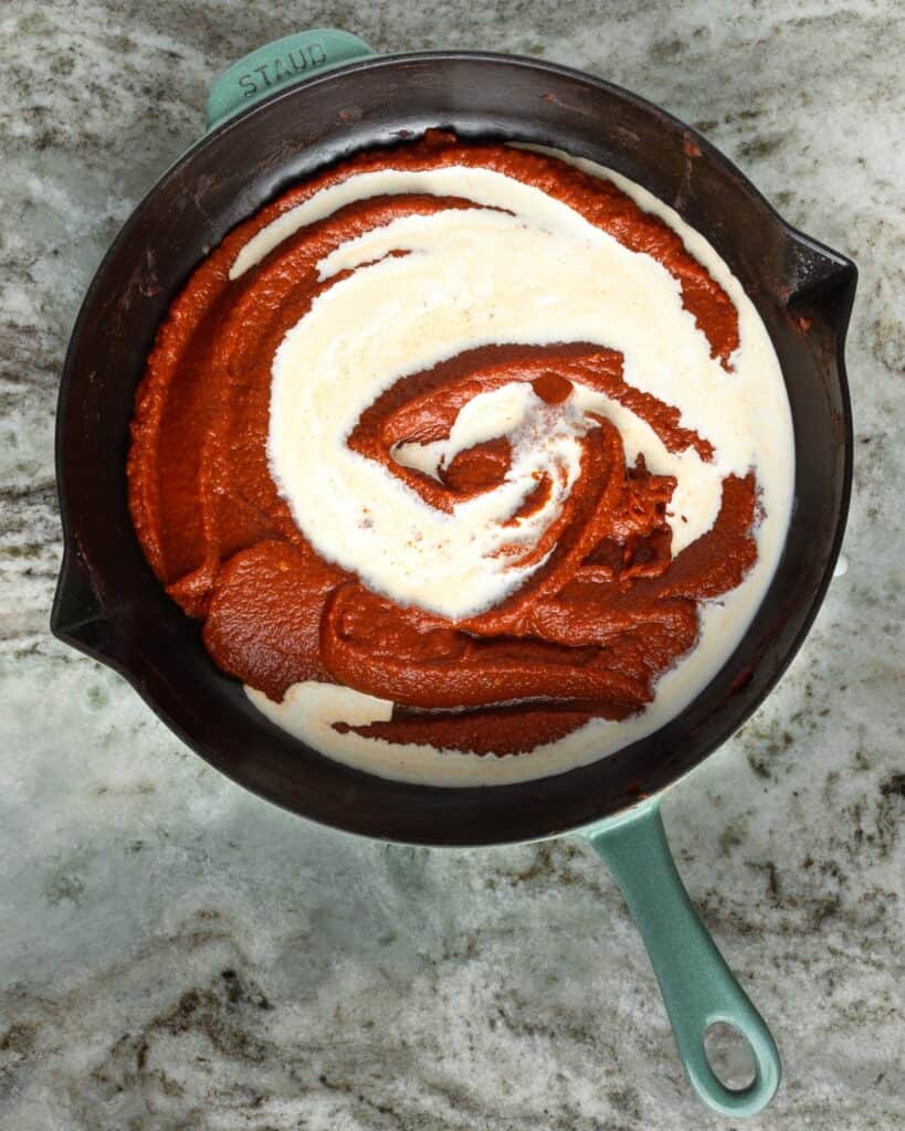 heavy cream poured over the tomato paste mixture in a skillet