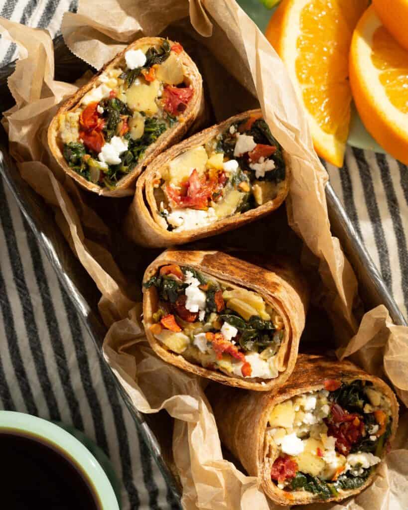 4 spinach and feta wraps cut in half in a container with orange slices and coffee