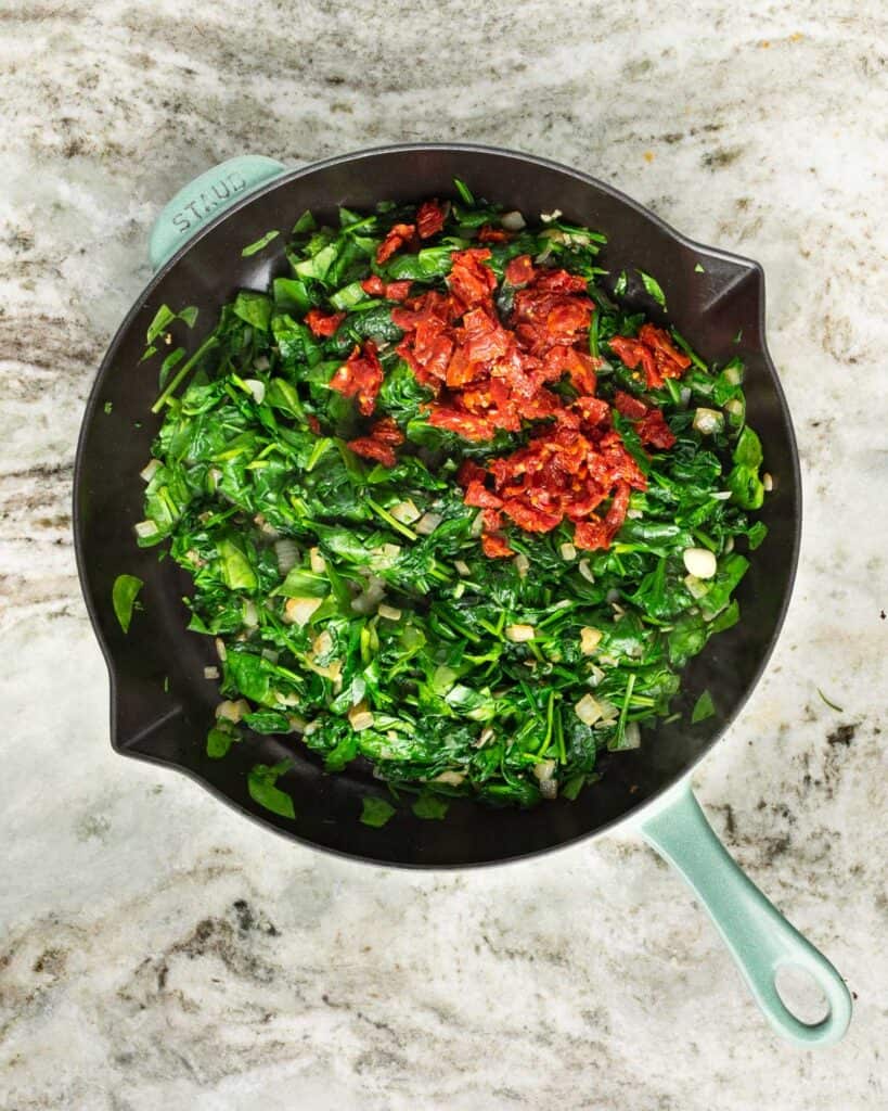 wilted spinach and sun dried tomatoes in a skillet