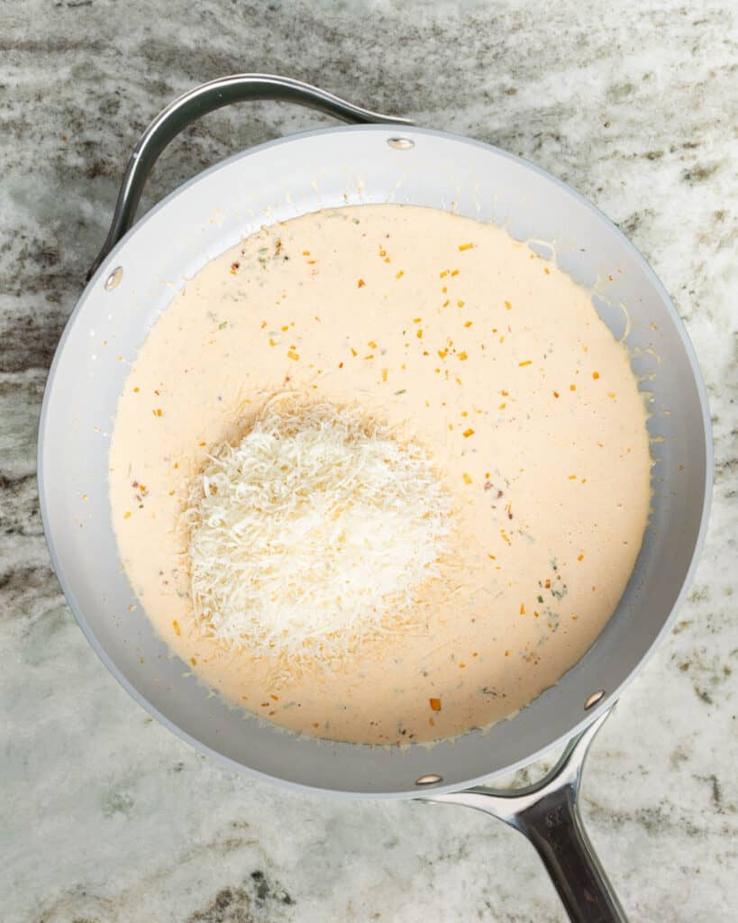 A saucepan with parmesan cheese added to cream sauce