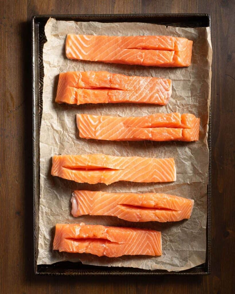 Salmon filets with slits on a parchment lined baking sheet.