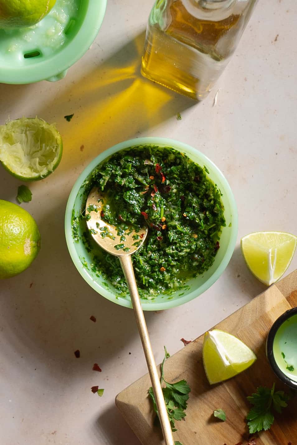 Chimichurri sauce in a green bowl with lime wedges around it.