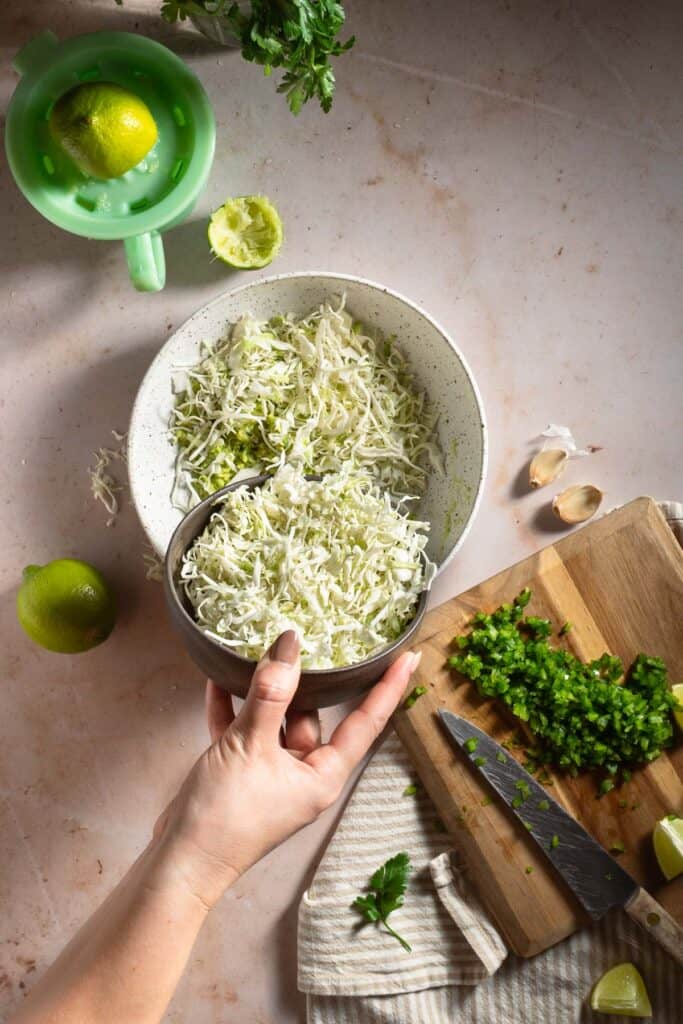 Adding shredded cabbage to a white bowl with mashed avocados.