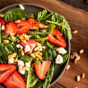 A bowl of strawberry and goat cheese salad with walnuts on a wooden cutting board.