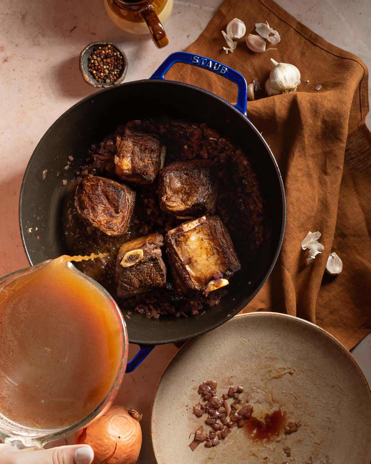 Pouring broth into a Dutch oven with seared short ribs.