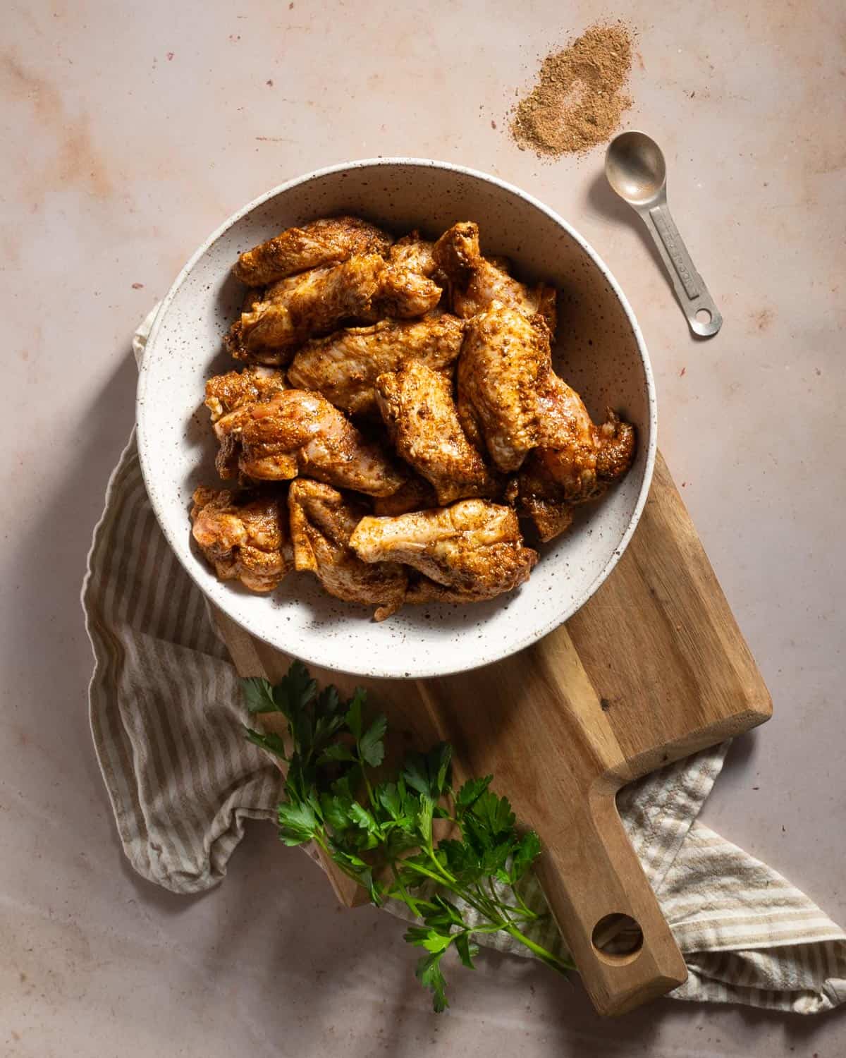 Raw chicken wings tossed in seasoning in a white bowl.