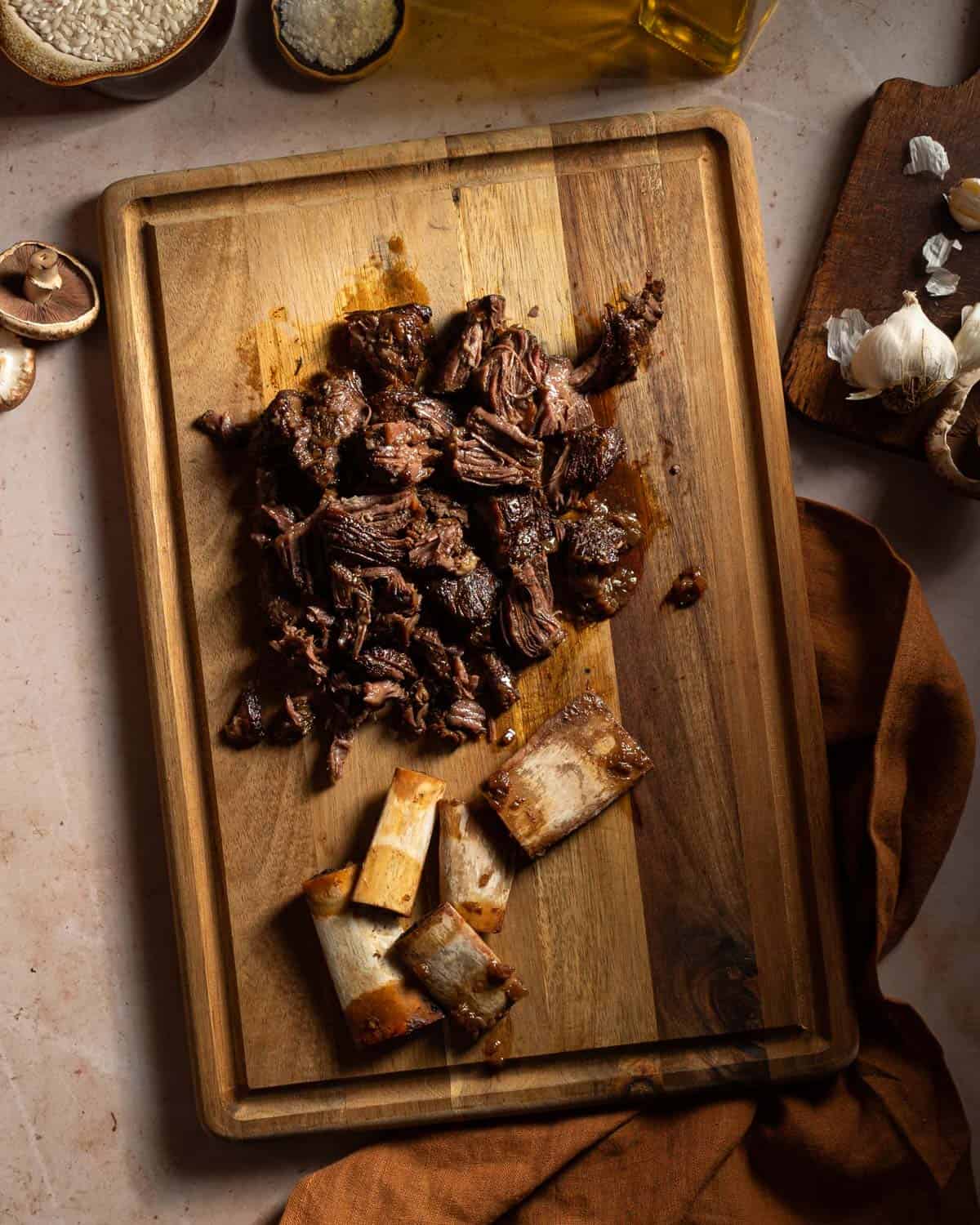 Chopped up braised short ribs on a cutting board with the bones removed.