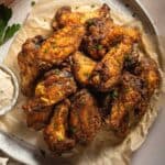 A plate of blackened crispy chicken wings topped with parsley and a side of cajun ranch.