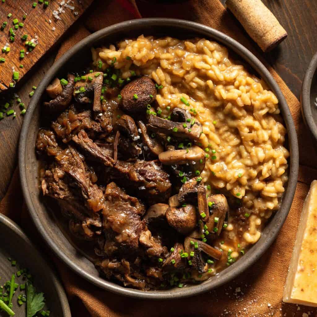 Braised short ribs with mushrooms and risotto topped with chives in a bowl.