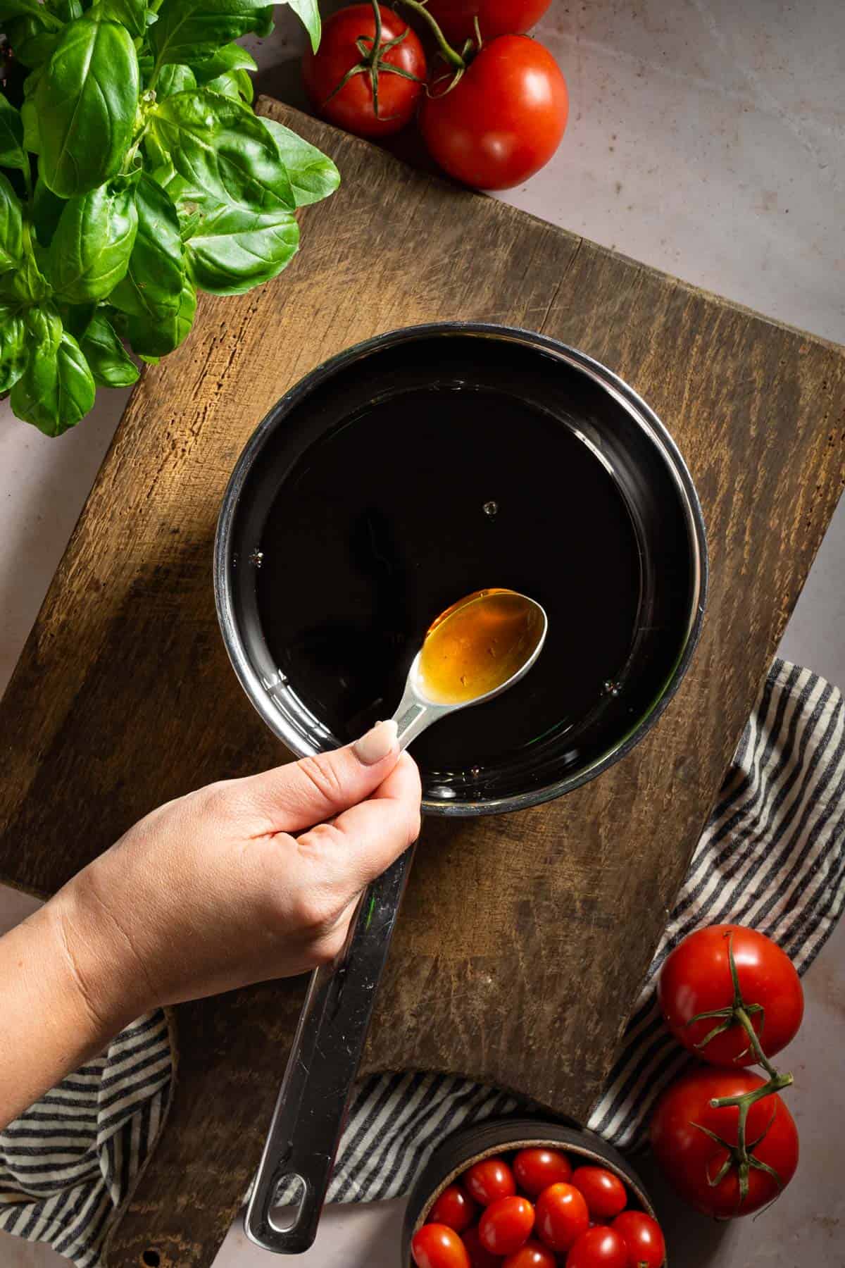 A hand adding honey to balsamic vinegar in a pot.