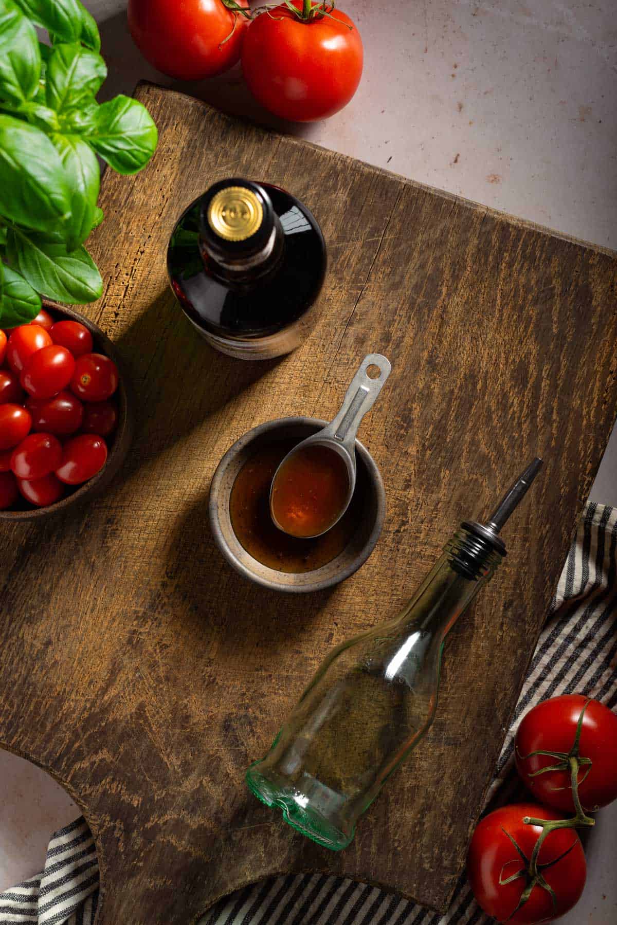 A cutting board with a bottle of balsamic vinegar and honey next to tomatoes and basil.