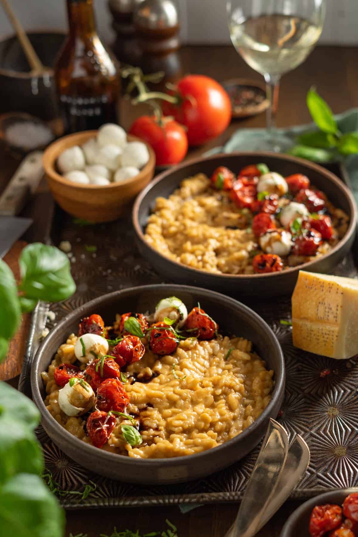 Two bowls of caprese risotto on a table with wine and parmesan cheese.
