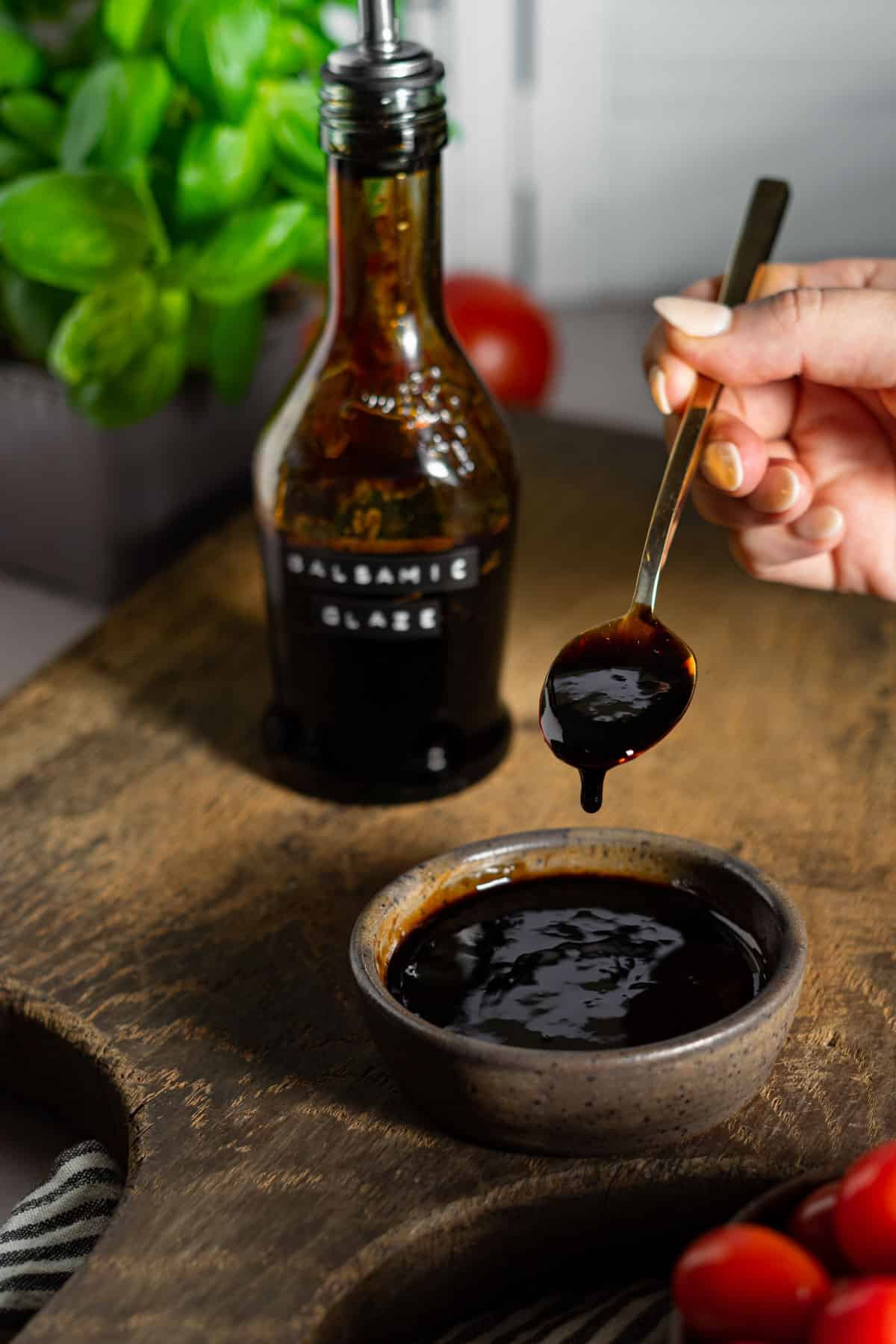 A spoon drizzling balsamic glaze into a small bowl.