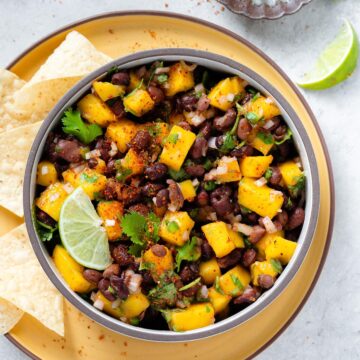 A bowl of black bean and mango salsa with limes.