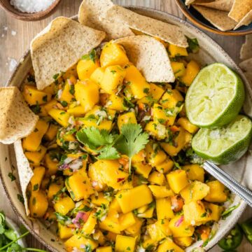 A large bowl of mango salsa with chips and limes.