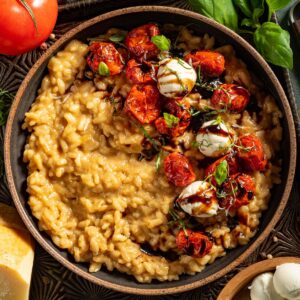 A bowl of risotto with roasted tomatoes, mozzarella balls, basil and balsamic glaze.