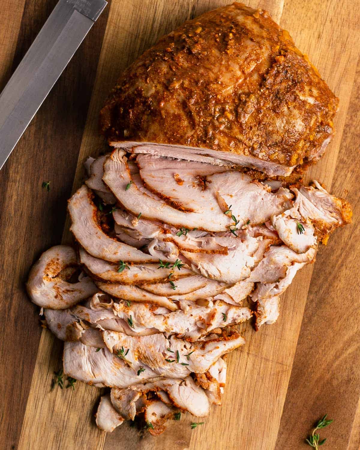 Sous vide cajun turkey breast sliced on a cutting board with a knife.