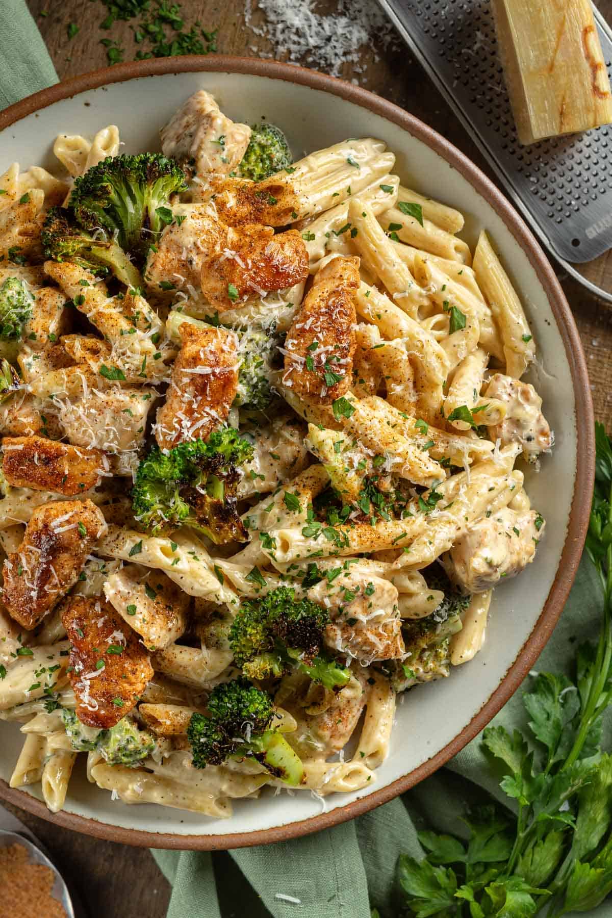 Up close of a large serving bowl of Cajun Chicken and Broccoli Alfredo topped with parsley and parmesan.