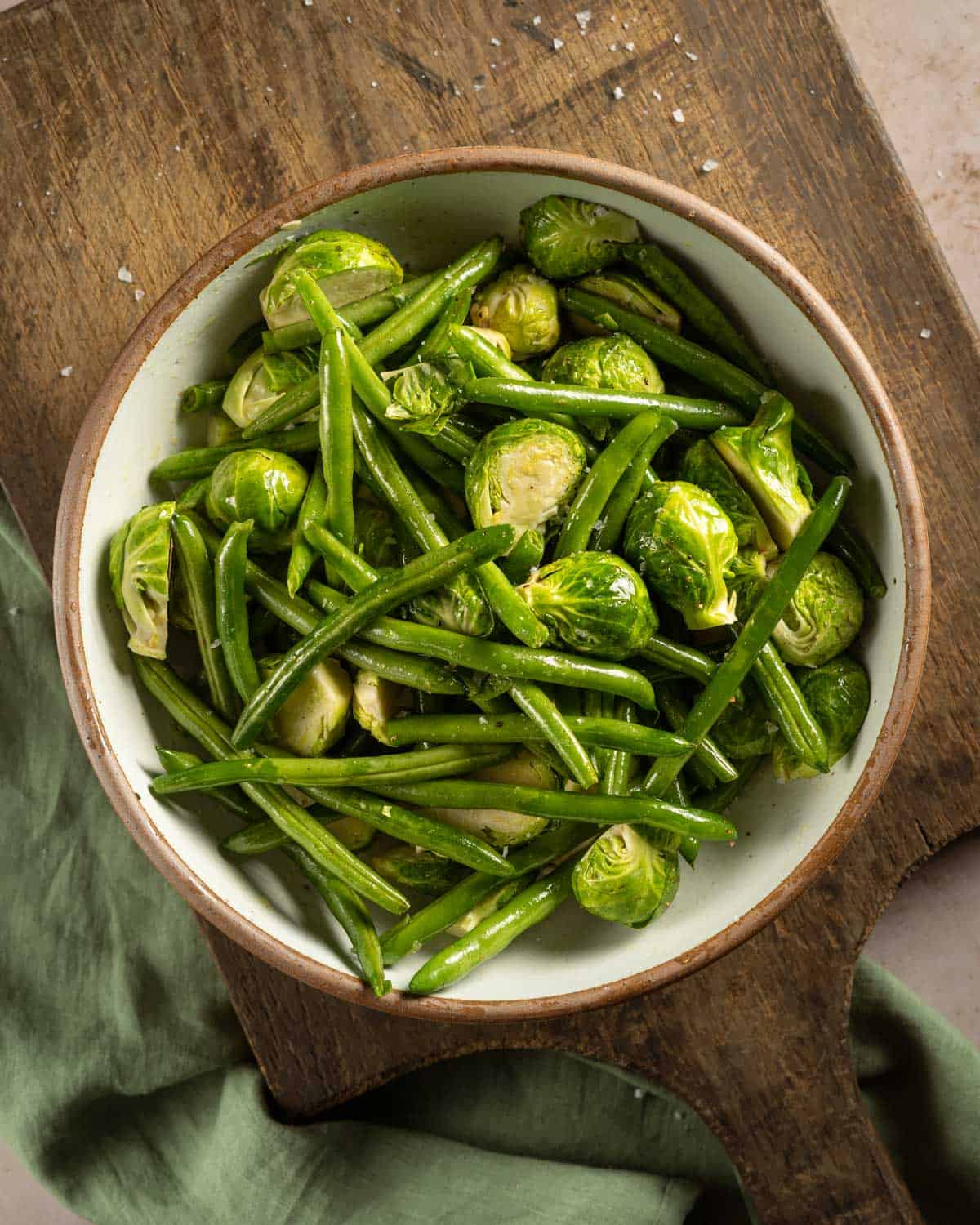 Green beans and brussel sprouts in a bowl tossed with salt and pepper.