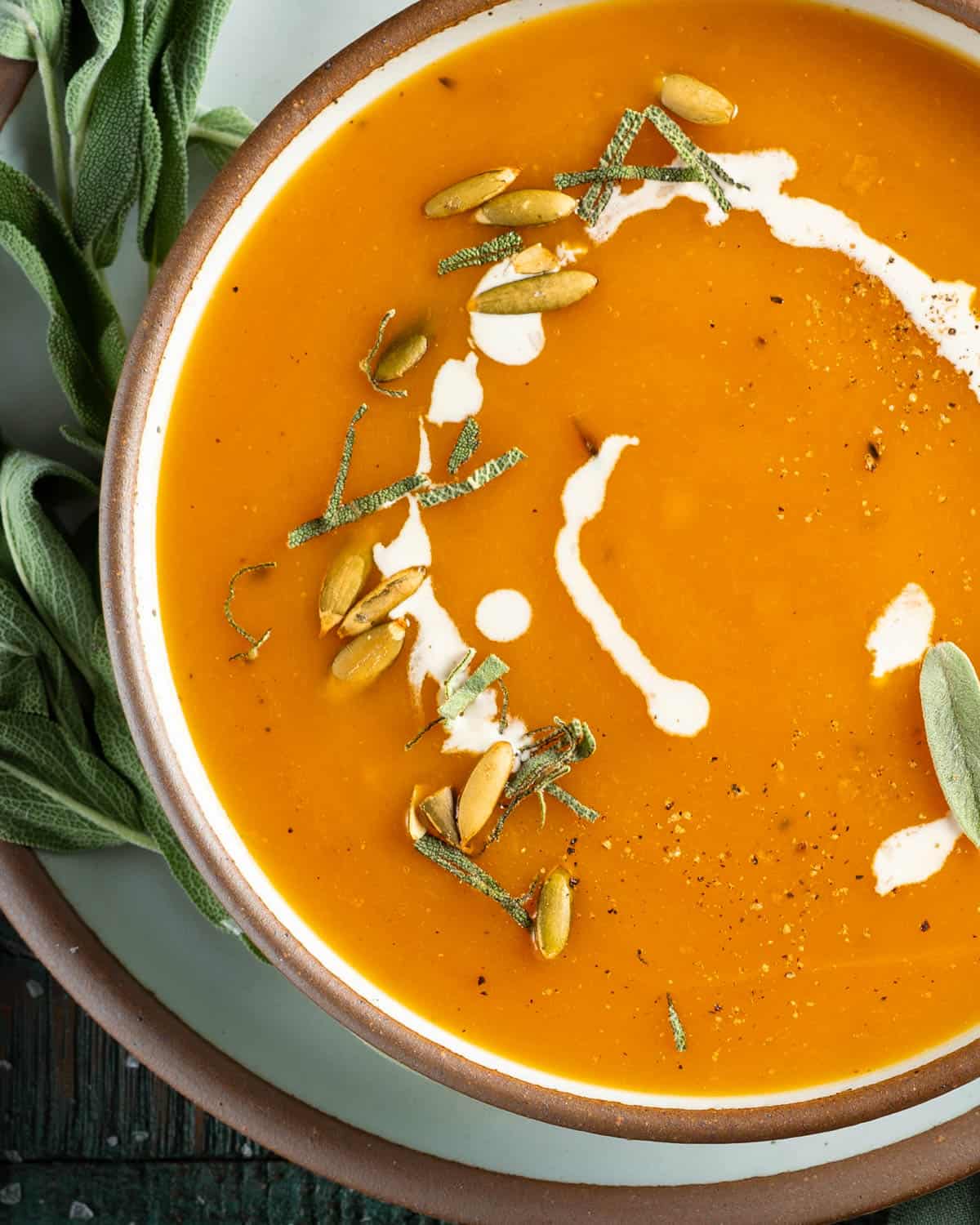 Up close bowl of butternut squash soup with toasted pumpkin seeds and sage.