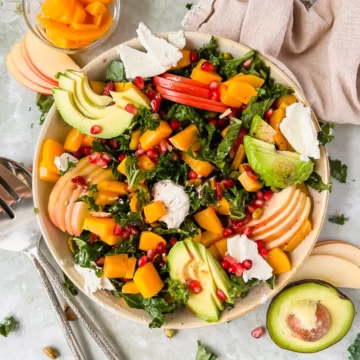 A large bowl of Fall Kale Salad with Roasted Butternut Squash and topped with pomegranate seeds.