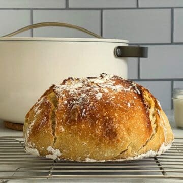 A loaf of sourdough bread on a counter next to a dutch oven.