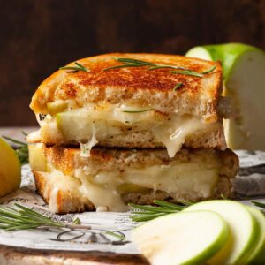 Brie and Apple Grilled Cheese on parchment paper with rosemary sprigs.