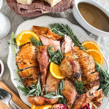 Roasted turkey in pieces on a platter with fresh herbs.