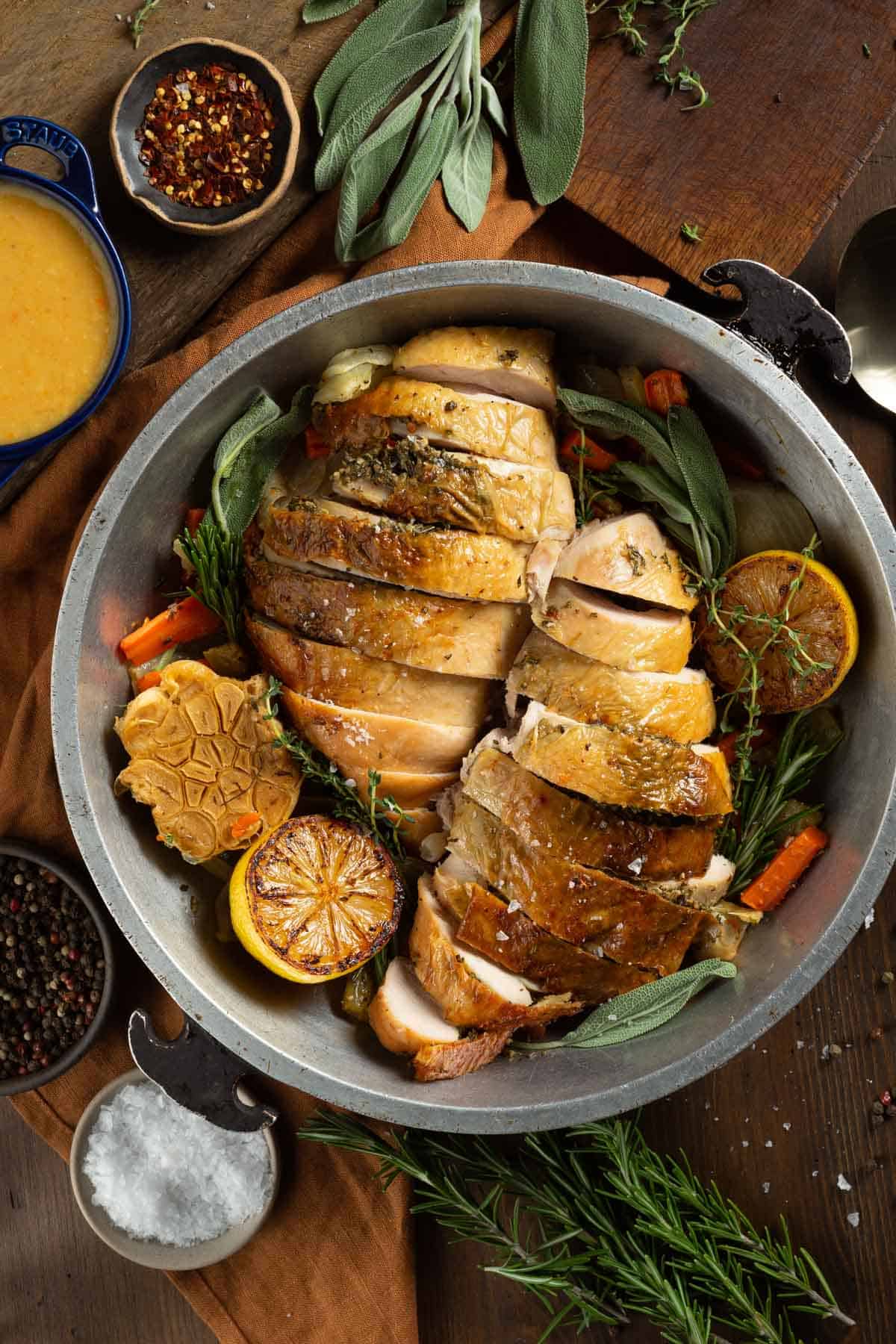 Sliced roasted turkey breast in a serving platter with fresh herbs and roasted vegetables.