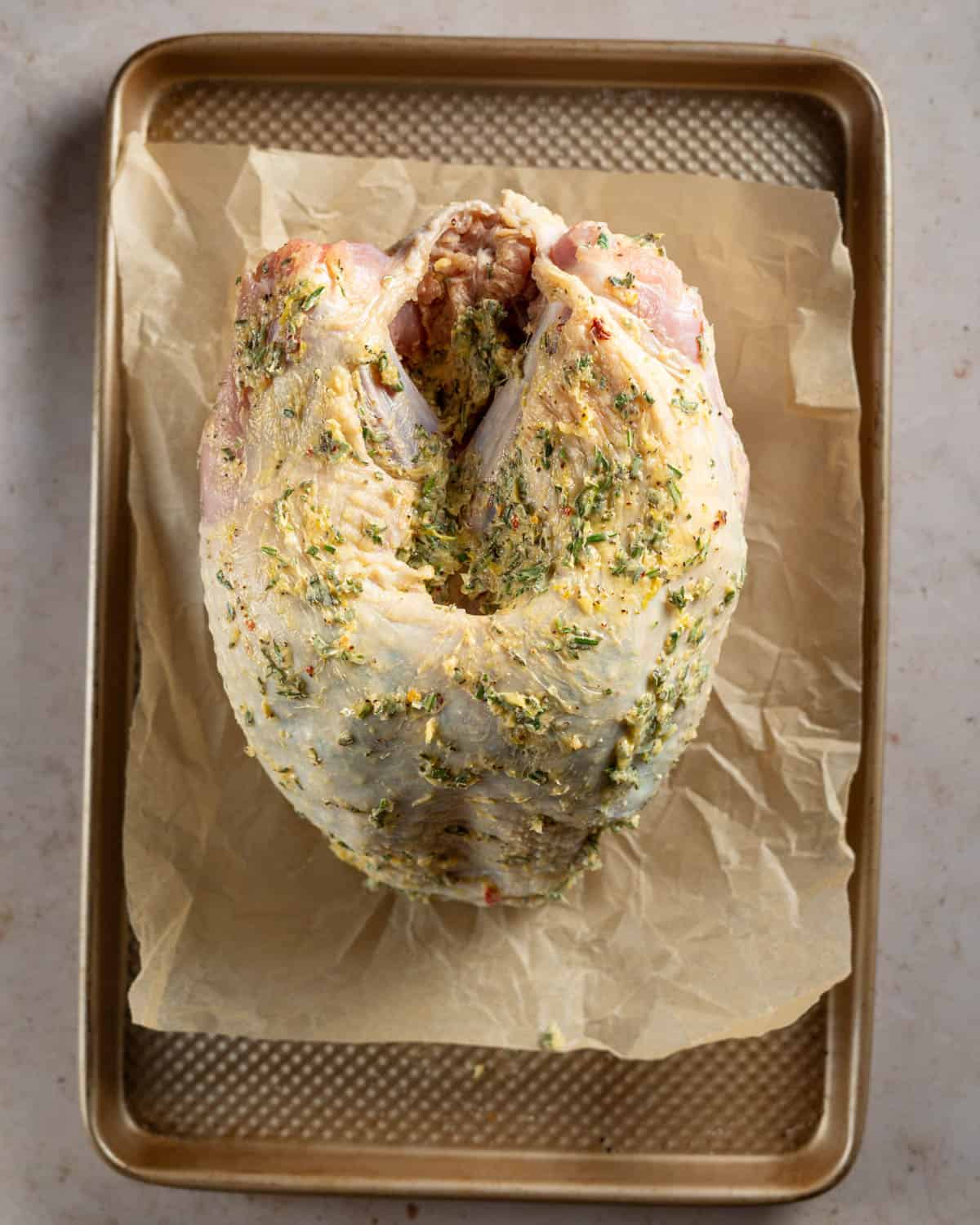 Turkey breast coated in garlic and herb butter on a baking sheet.