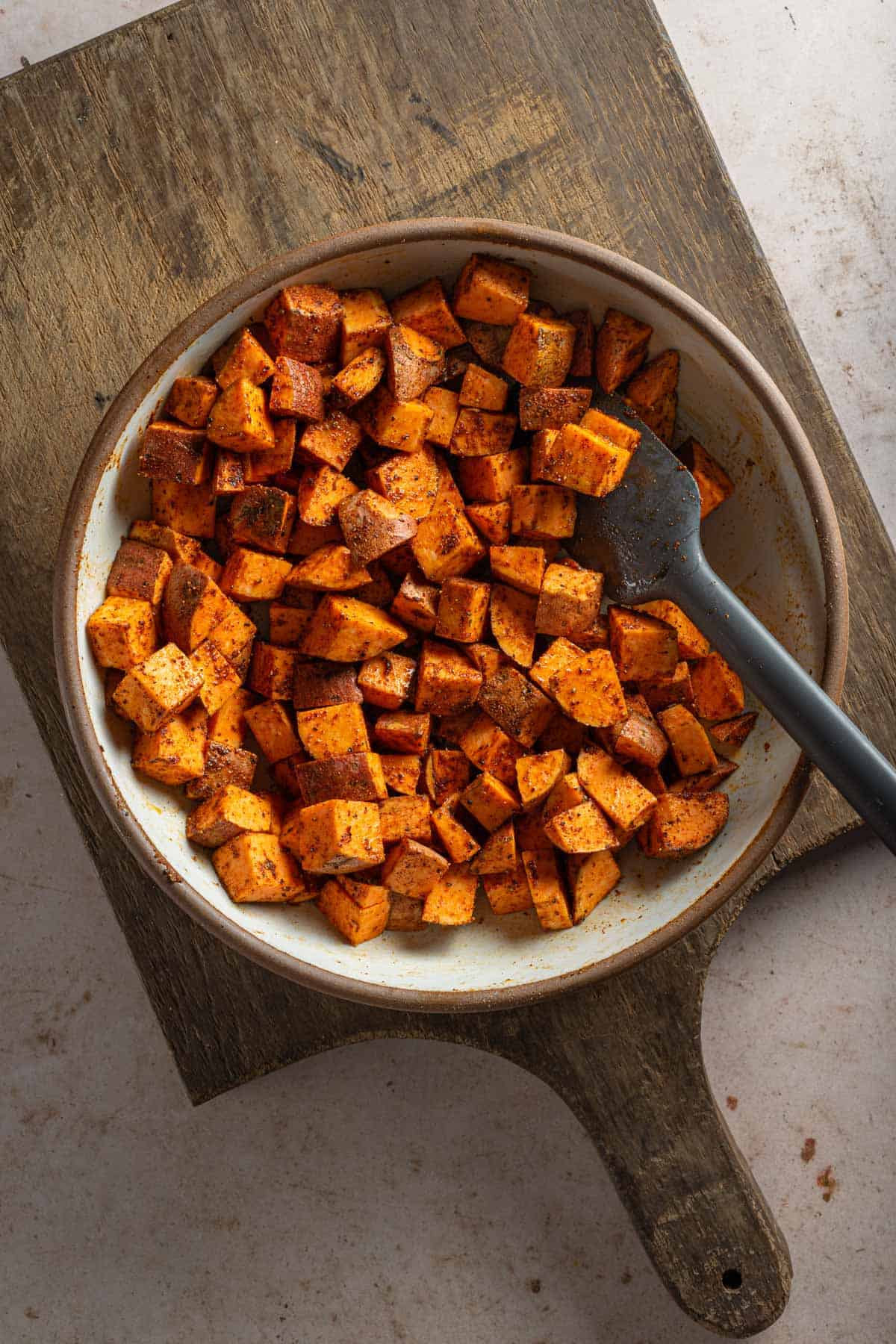 A bowl with sweet potato cubes tossed with seasonings.